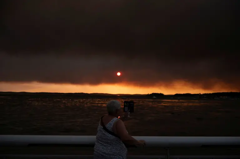 This-picture-shows-a-woman-watching-smoke-from-the-beach-in-Andernos-Les-Bains-during-a-fire-in-Lege-Cap-Ferret-forest-southwestern-France-on-July-23-2026-as-part-of-the-nearby-area-has-been-evacuated-A-highly-virulent-wildfire-has-swept-through-more-than-3700-hectares-since-July-22-2026-near-the-Arcachon-Basin-Gironde-where-nearly-20-000-residents-and-tourists-have-been-evacuated-in-total-from-this-area-of-the-Landes-de-Gascogne-forest-already-devastated-by-flames-in-2022