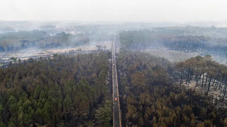This-aerial-view-shows-cars-driving-past-a-burnt-area-as-smoke-rises-following-a-wildfire-in-Le-Porge-in-the-Gironde-Department-south-western-France-on-July-25-2026-The-fires-which-are-on-an-unprecedented-scale-and-have-forced-the-evacuation-of-around-200-000-fire-refugees-in-Gironde-and-the-Landes-were-still-not-under-control-on-July-25-2026-and-continue-to-keep-firefighters-and-military-personnel-on-high-alert-including-an-A400M-aircraft-deployed-to-tackle-the-blaze-for-the-first-time