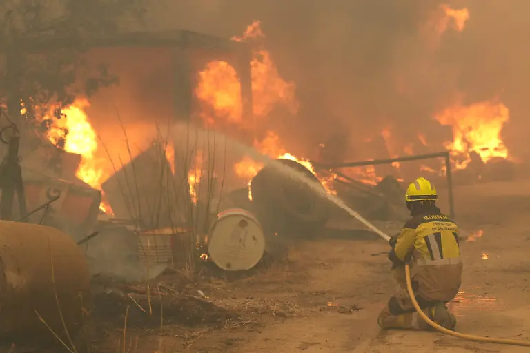 A-firefighter-waters-burning-tires-and-barrels-while-battling-a-wildfire-in-Cebreros-area-near-Avila-80-kms-west-of-Madrid-on-July-24-2026-The-worst-wildfires-in-the-Madrid-region-s-history-rage-west-of-the-Spanish-capital-forcing-authorities-to-evacuate-or-order-around-40-000-people-to-remain-indoors