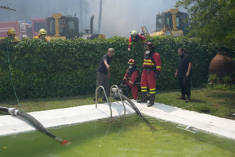 Firefighters-collect-water-from-a-swimmming-pool-while-battling-a-fire-surrounding-La-Atalaya-residential-area-in-El-Tiemblo-80-kms-west-of-Madrid-on-July-25-2026-amid-wildfires-that-have-burned-up-to-25-000-hectares-Spanish-firefighters-hoped-to-get-control-of-wildfires-raging-near-Madrid-on-Saturday-but-an-official-warned-that-erratic-winds-threatened-to-fan-the-blazes-further-The-worst-wildfires-in-the-Madrid-region-s-history-rage-west-of-the-Spanish-capital-forcing-authorities-to-evacuate-or-order-around-60-000-people-to-remain-indoors