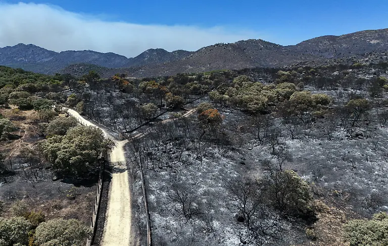 This-picture-shows-an-aerial-view-of-scorched-ground-in-the-Camino-de-Navahonda-area-following-a-wildfire-near-Robledo-de-Chavela-60-kilometers-west-of-Madrid-on-July-27-2026-Spain-faces-two-crucial-days-to-bring-raging-wildfires-under-control-before-weather-conditions-worsen-authorities-said-on-July-27-2026-though-they-were-making-some-progress-and-planned-to-start-returning-evacuees-to-certain-areas-The-fires-in-the-Iberian-country-have-affected-an-area-of-77-000-hectares-190-000-acres-nearly-the-size-of-New-York-City-according-to-the-authorities-Since-the-start-of-the-year-fires-in-Spain-have-ravaged-150-000-hectares-and-killed-13-people