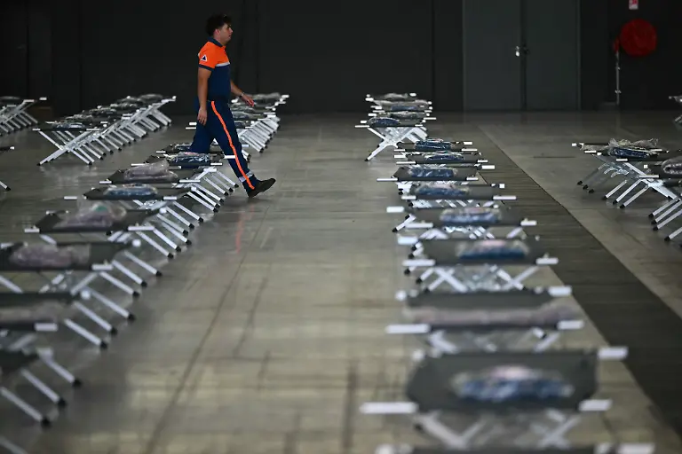 A-member-of-the-civil-protection-walks-besides-set-up-beds-at-the-MEETT-Toulouse-Exhibition-and-Convention-Centre-used-to-host-people-displaced-by-the-wildfires-in-the-Gironde-region-in-Aussonne-near-Toulouse-south-western-France-on-July-28-2026-Over-the-past-six-days-the-wildfire-near-Bordeaux-has-ravaged-42-000-hectares-103-000-acres-forced-220-000-people-to-flee-and-destroyed-240-houses-Firefighters-said-on-July-28-2026-the-fire-had-not-expanded-overnight-as-they-managed-to-tackle-several-flareups-The-fires-burning-in-Spain-and-France-advanced-quickly-because-of-tinderbox-conditions-worsened-by-successive-heatwaves-the-two-countries-have-experienced-since-May-The-current-European-drought-was-made-more-severe-by-human-caused-climate-change-scientists-from-the-World-Weather-Attribution-group-said-in-a-study-published-last-week