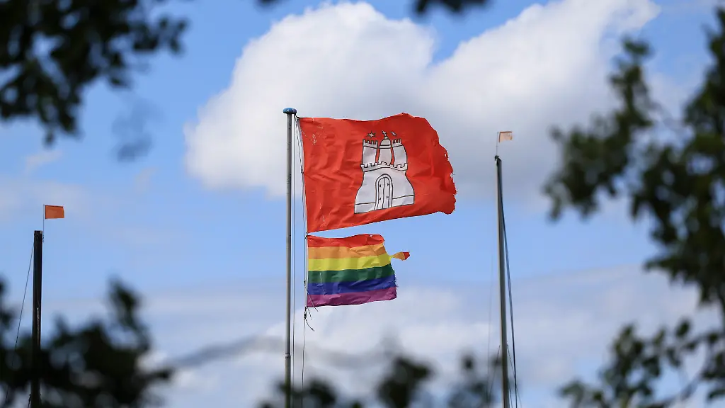 Eine-Regenbogenfahne-und-eine-Flagge-mit-dem-Wappen-von-Hamburg-haengen-am-Fahnenmast-eines-Bootsverleihs-an-der-Alster-Nach-dem-mutmasslich-islamistisch-motivierten-Angriff-auf-feiernde-Menschen-beim-Christopher-Street-Day-CSD-in-Berlin-will-die-Hamburger-Polizei-die-geplante-Grossdemonstration-der-queeren-Community-am-kommenden-Samstag-mit-mehr-Personal-schuetzen