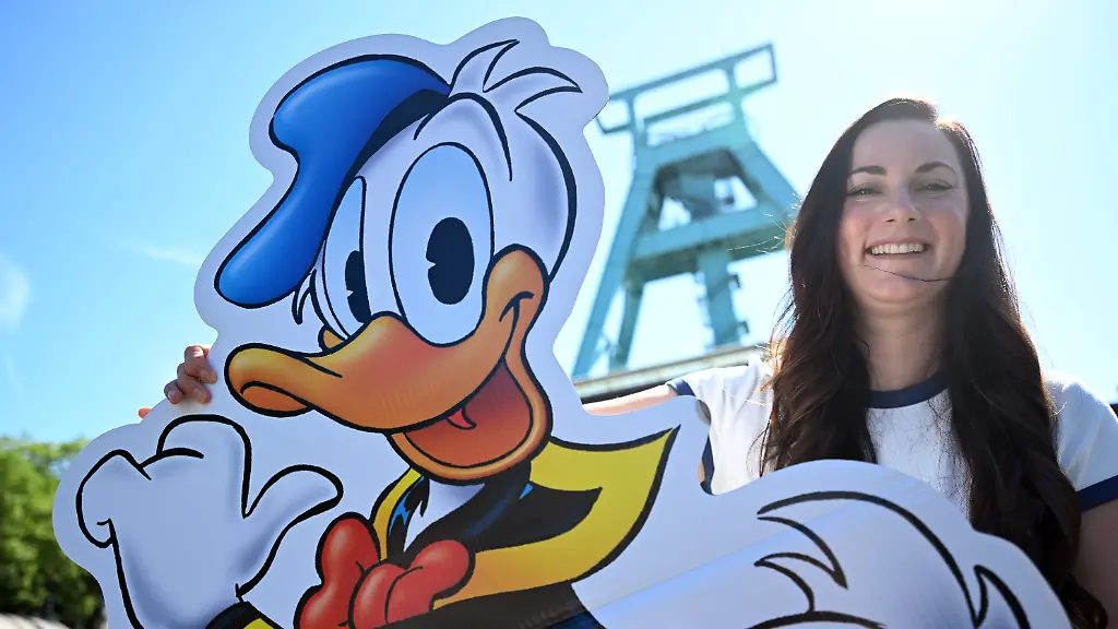 28-07-2026-Nordrhein-Westfalen-Bochum-Cynthia-L-Pineda-Disney-Zeichnerin-steht-mit-einer-Donald-Duck-Figur-vor-dem-Deutschen-Bergbau-Museum-Donald-Duck-erkundet-als-radelnder-Reporter-fuer-den-Entenhausener-Kurier-zwischen-Dortmund-und-Duisburg-den-Pott-Die-Ruhrgebietsausgabe-des-Micky-Maus-Magazins-wurde-vorgestellt