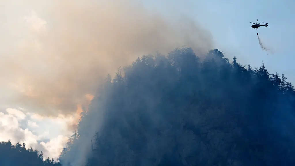 Ein-Hubschrauber-laesst-zur-Bekaempfung-eines-Brandes-im-Bergwald-in-den-Chiemgauer-Alpen-Loeschwasser-ab