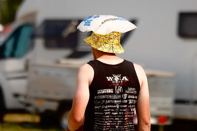 Ein-Festivalbesucher-geht-mit-einem-Beutel-Eiswuerfeln-auf-dem-Kopf-ueber-das-Festival-Gelaende-beim-Wacken-Open-Air-W-O-A-Das-W-O-A-gilt-als-groesstes-Heavy-Metal-Festival-der-Welt