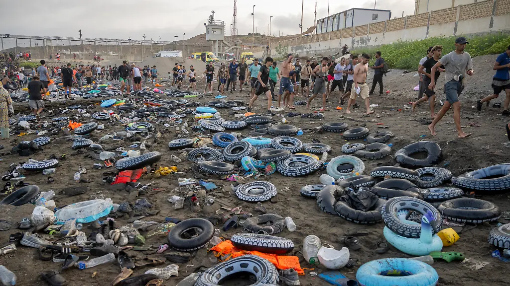 Bootsfluechtlinge-und-Migranten-gehen-nach-dem-Ueberqueren-der-Grenze-zwischen-Ceuta-und-Marokko-hinter-Schwimmreifen-Auch-bei-Einbruch-der-Dunkelheit-am-Donnerstag-dem-30-Juli-stroemten-weiterhin-zahlreiche-Menschen-unkontrolliert-aus-Marokko-nach-Ceuta-Seit-den-fruehen-Morgenstunden-hatten-Tausende-von-Migranten-die-autonome-Stadt-erreicht-indem-sie-schwimmend-oder-zu-Fuss-die-Mole-umgingen-die-die-autonome-Stadt-von-Marokko-trennt