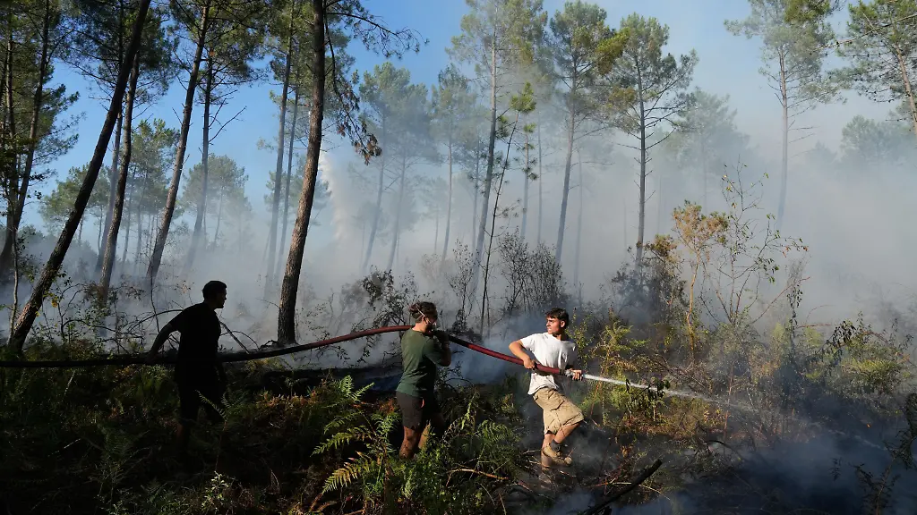 A-group-hold-a-firehose-and-try-to-suppress-a-fire-near-Lacanau-as-wildfires-rage-outside-Bordeaux-France-Monday-July-27-2026