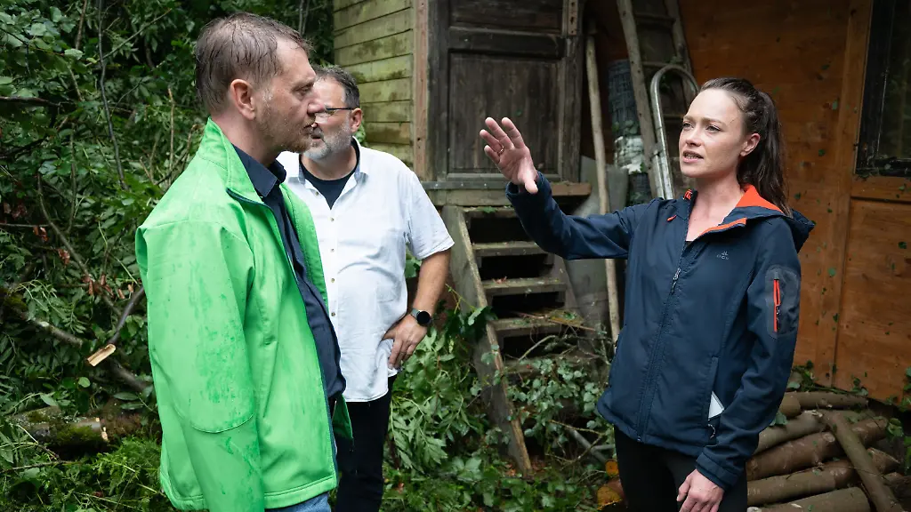 01-08-2026-Sachsen-Rathen-Michael-Kretschmer-CDU-l-Ministerpraesident-von-Sachsen-spricht-im-Amselgrund-im-Nationalpark-Saechsische-Schweiz-mit-der-TV-und-Eventkoechin-Verena-Leister-Das-Unwetter-hat-den-Imbiss-der-TV-Koechin-zerstoert