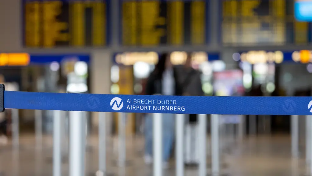Absperrband-mit-Logo-des-Albrecht-Duerer-Airport-Nuernberg-im-Terminal-Im-unscharfen-Hintergrund-sind-Abflugtafeln-und-Bereiche-des-Flughafenbetriebs-zu-sehen-Eroeffnung-der-neuen-CT-Kontrollstelle-am-Airport-Nuernberg-Nuernberg-08-05