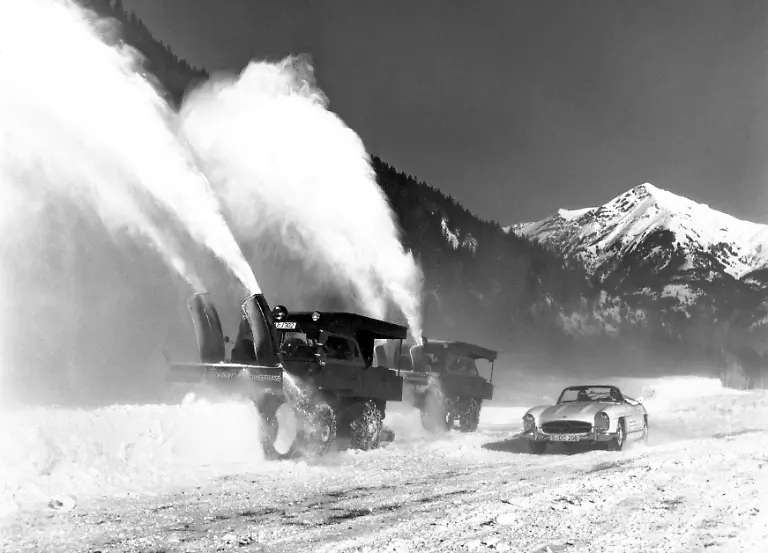 Zwei-Mercedes-Benz-Unimog-der-Baureihe-411-mit-Schneefraese-angetrieben-von-einem-zusaetzlichen-Motor-auf-der-Pritsche-Im-Vordergrund-ein-Mercedes-Benz-300-SL-Roadster-W-198