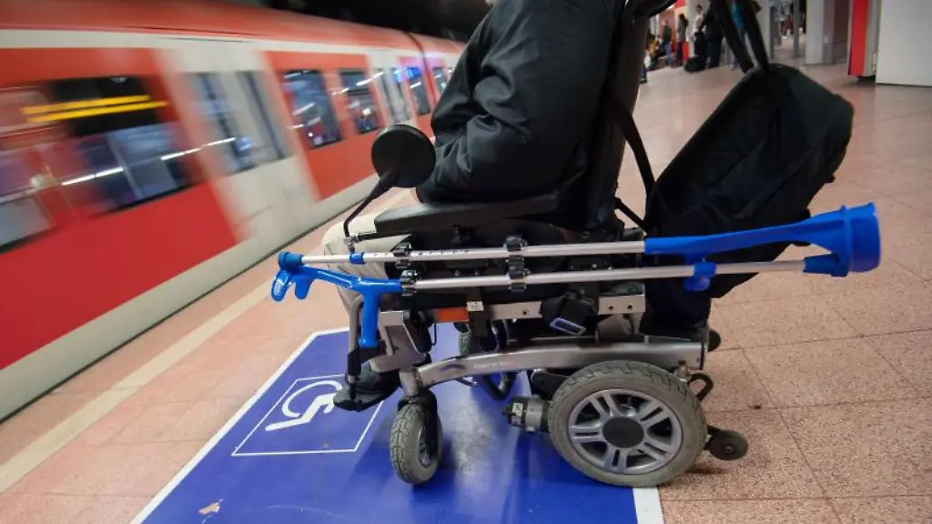 Ein-Mann-sitzt-mit-seinem-Elektro-Rollstuhl-an-einem-Bahnhof-am-Gleis