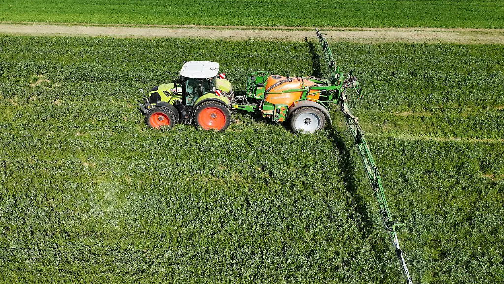 Themenfoto-Landwirtschaft-Duengen-Pestizide-Ein-Landwirt-faehrt-mit-seinenm-Traktor-ueber-ein-gruenes-Feld-und-duengt-mit-Pestiziden
