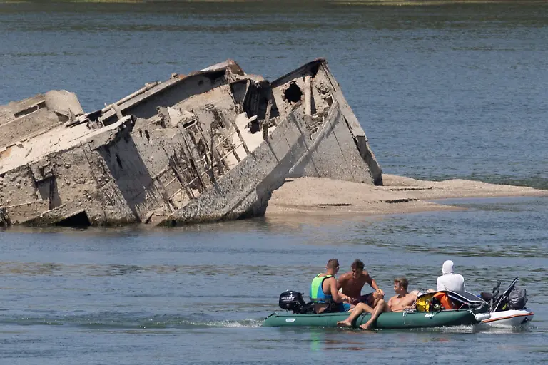 People-in-a-boat-pass-by-a-sunken-German-warship-from-World-War-II-exposed-due-to-low-Danube-River-levels-caused-by-drought-and-extreme-heat-in-Prahovo-Serbia-July-30-2026