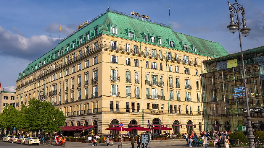 Aussenansicht-des-Hotel-Adlon-Kempinski-am-Pariser-Platz-in-Berlin-Mitte-nahe-dem-Brandenburger-Tor-Die-historisierende-Fassade-mit-gruenem-Kupferdach-und-roter-Aussengastronomie-Rechts-die-Akademie-der-Kuenste-Zahlreiche-Besucher-beleben-den-Platz-Hotel-Adlon-Kempinski-Berlin-Luxushotel-am-Pariser-Platz-Berlin-10-05