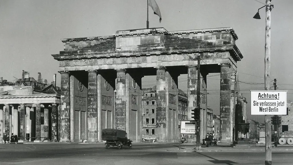Berlin-Mitte-Kriegsende-Sektorengrenze-West-Berlin-Das-Brandenburger-Tor-zu-Zeiten-vor-dem-Bau-der-Berliner-Mauer-mit-einem-Warnschild-im-Vordergrund-um-1948