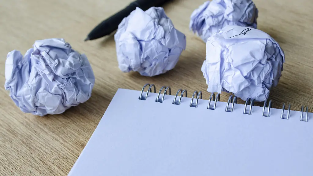 Ein-Schreibtischarrangement-mit-mehreren-zerknitterten-Papierstuecken-und-einem-leeren-Notizblock-das-Frustration-kreativen-Kampf-und-den-Prozess-der-Verfeinerung-von-Ideen-vermittelt