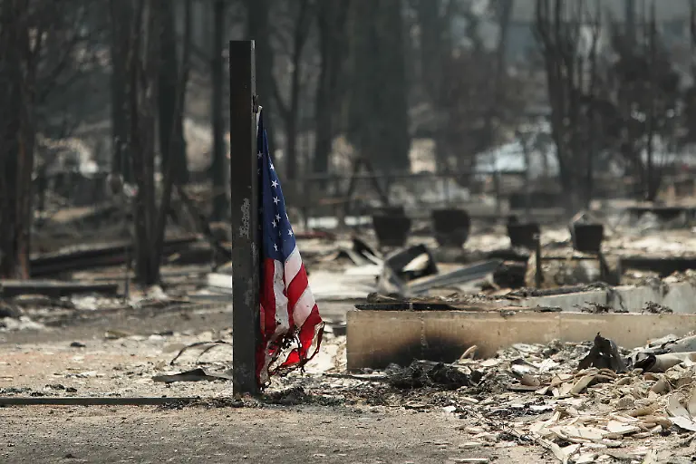 An-American-flag-stands-at-a-burned-structure-in-a-residential-area-of-Westgate-after-a-wildfire-Monday-Aug-3-2026-in-Spokane-Wash