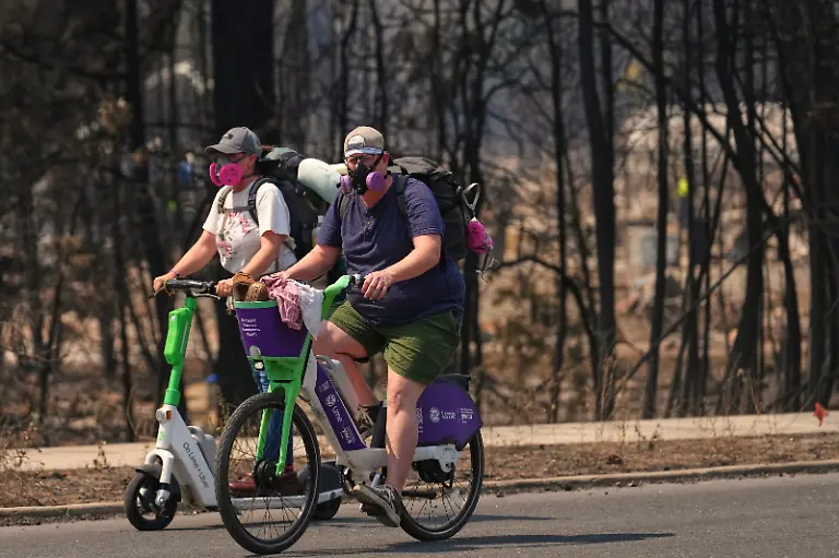 Wearing-protective-masks-against-smoke-Tim-Lindblade-right-and-Donna-Fifield-left-carry-possessions-retrieved-from-Lindblade-s-home-while-riding-a-Lime-scooter-and-bike-back-to-a-checkpoint-after-a-wildfire-hit-the-northwest-part-of-Spokane-Wash-Tuesday-Aug-4-2026