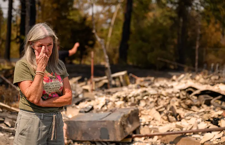 A-woman-reacts-as-she-views-her-daughter-s-home-burned-during-the-Old-Trails-fire-in-Spokane-Washington-on-August-4-2026-Emergency-crews-on-Tuesday-were-racing-to-contain-flames-in-the-US-Northwest-where-a-man-was-arrested-on-suspicion-of-arson-in-connection-with-the-largest-of-the-fires-that-have-displaced-tens-of-thousands-Wildfires-supercharged-by-drought-and-intense-heat-have-torn-through-the-city-of-Spokane-in-Washington-state-burning-thousands-of-acres-and-reducing-hundreds-of-buildings-to-cinders-while-anxious-families-await-news-on-when-they-can-return