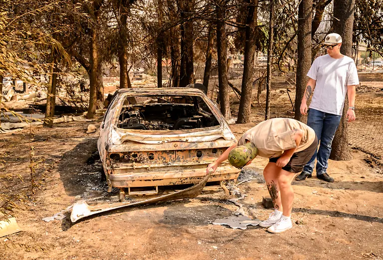 Residents-look-at-their-burned-Mustang-after-the-Old-Trails-Fire-in-Spokane-Washington-on-August-4-2026-US-authorities-arrested-a-man-on-August-3-2026-on-suspicion-of-arson-in-connection-with-the-biggest-of-three-fires-burning-around-the-northwestern-city-of-Spokane-as-firefighters-raced-to-contain-flames-that-have-displaced-tens-of-thousands-Wildfires-supercharged-by-drought-and-intense-heat-have-torn-through-the-city-in-Washington-state-burning-thousands-of-acres-and-reducing-hundreds-of-buildings-to-cinders-while-anxious-families-await-news-on-when-they-can-return