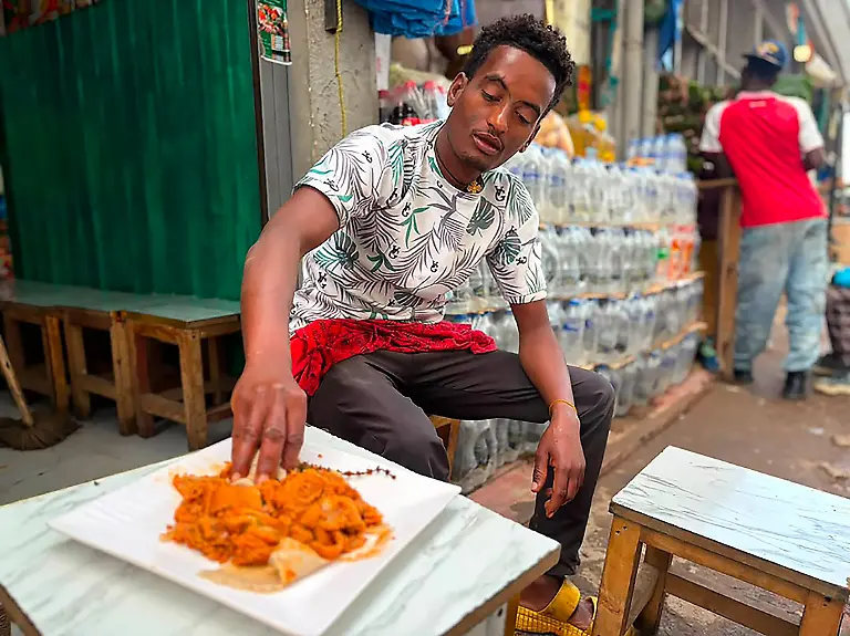 Fantahun-Hailu-fruehstueckt-Fir-Fir-im-Vorort-Ayat-in-der-aethiopischen-Hauptstadt-Addis-Abeba-Die-Basis-des-Fruehstuecks-Gerichts-ist-zerkleinertes-Injera-das-beruehmte-sauer-weiche-Fladenbrot-der-aethiopischen-Kueche-vermengt-mit-gewuerztem-Butterschmalz-Chili-Paste-und-Eintopf-Resten-aus-Gemuese-und-Fleisch