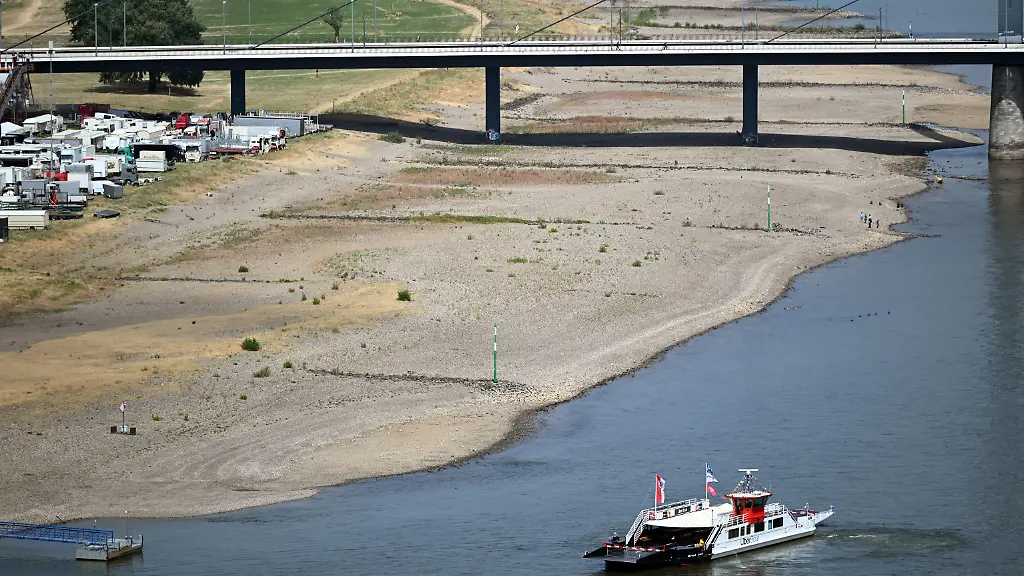 ARCHIV-24-07-2026-Nordrhein-Westfalen-Duesseldorf-Ein-Schiff-faehrt-am-Rheinufer-entlang-Aufgrund-der-Trockenheit-fuehrt-der-Rhein-weniger-Wasser