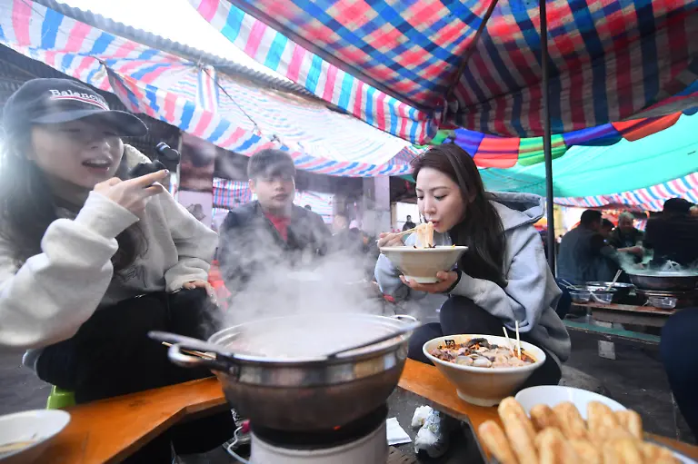 241120-LIUZHOU-Nov-20-2024-A-tourist-1st-R-from-east-China-s-Zhejiang-Province-has-breakfast-at-a-morning-market-in-Chengtuan-Town-of-Liuzhou-south-China-s-Guangxi-Zhuang-Autonomous-Region-Nov-20-2024-With-various-choices-delicious-taste-and-affordable-price-breakfast-at-the-morning-market-in-Chengtuan-Town-are-deeply-loved-by-local-residents-It-has-also-become-popular-on-the-internet-attracting-more-and-more-tourists-to-experience-its-unique