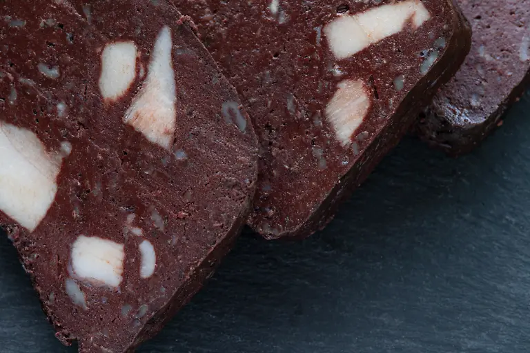 This-is-a-top-view-of-homemade-black-pudding-that-s-been-sliced-into-square-pieces-and-placed-on-a-black-slate-which-is-sitting-on-a-wooden-table