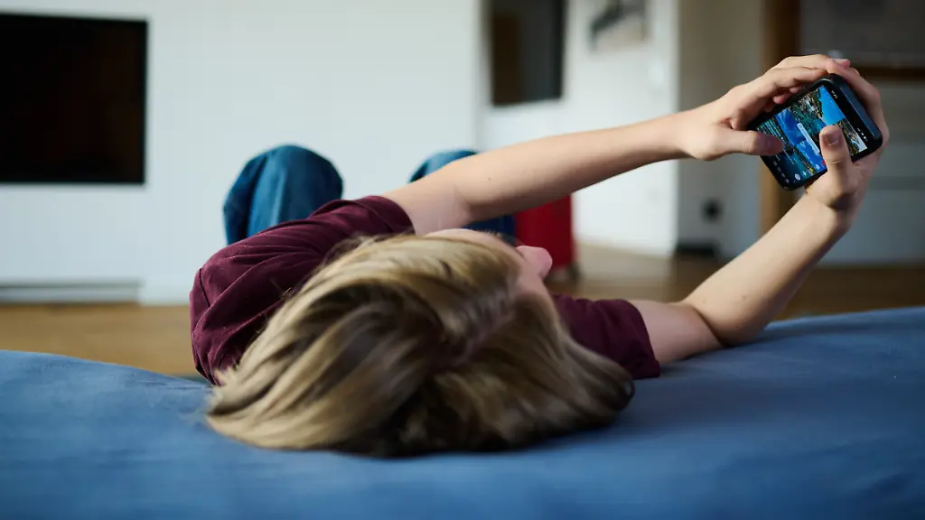 Ein-Teenager-guckt-auf-ein-Handy-waehrend-er-auf-einer-Matratze-liegt