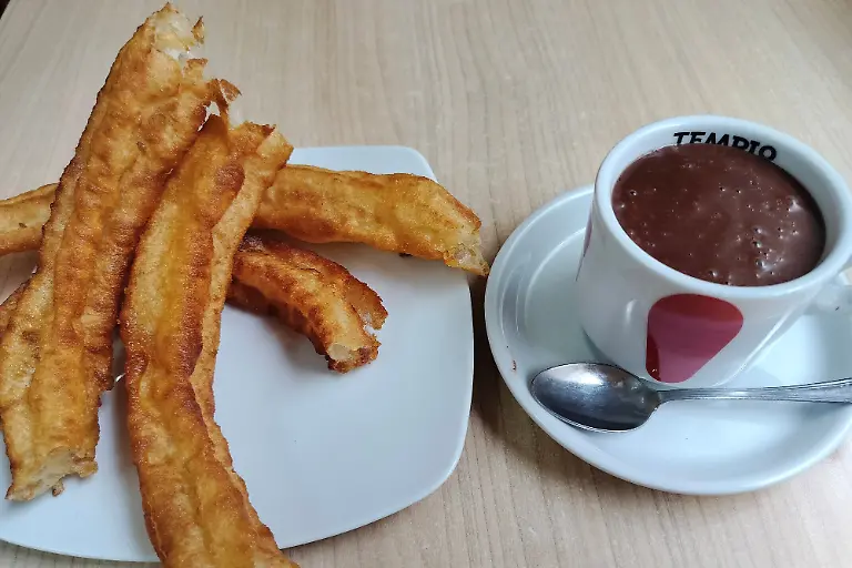 Churros-con-Chocolate-stehen-in-Madrid-auf-einem-Tisch-Das-Gericht-aus-frittiertem-Spritzgebaeck-Churros-und-einer-sehr-dickfluessigen-heissen-Trinkschokolade-zum-Dippen-wird-in-Spanien-gerne-zum-Fruehstueck-gegessen