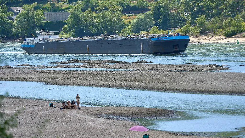 Touristen-entspannen-sich-auf-einer-Sandbank-im-Rhein-nahe-der-Loreley-waehrend-ein-Frachtschiff-vorbeifaehrt
