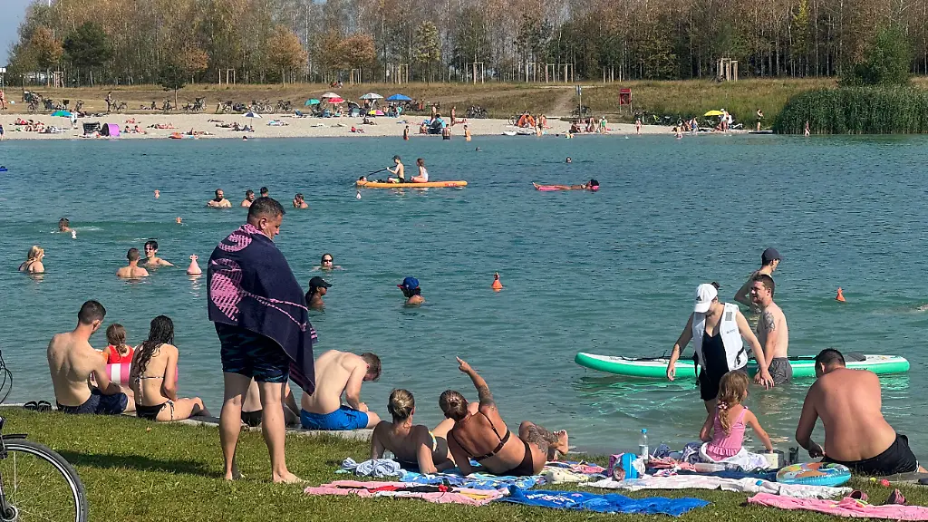 Wetterbid-vom-02-08-2026-Sommerstimmung-am-Riemer-See-Zahlreiche-Badegaeste-geniessen-das-sonnige-Wetter-und-die-angenehmen-Temperaturen-am-beliebten-Badesee-in-Muenchen-Riemer-See-in-Muenchen-an-einem-sonnigen-Sommertag-Viele-Menschen-schwimmen-im-klaren-Wasser-entspannen-auf-Handtuechern-am-Ufer-oder-geniessen-die-Sonne-am-Sandstrand-Im-Vordergrund-stehen-Fahrraeder-auf-der-Wiese-waehrend-Familien-Badegaeste-und-Wassersportler-fuer-eine-lebendige-Atmosphaere-sorgen-Der-blaue-Himmel-und-die-ruhige-Wasserflaeche-unterstreichen-das-warme-Sommerwetter-SVEN-SIMON-Fotoagentur-GmbH-Co-Pressefoto-KG-Seidlhofstr-10-85540-Haar-GLS-Bank-IBAN-DE75-4306-0967-4030-0251-00-BIC-GENODEM1GLS-www-svensimon