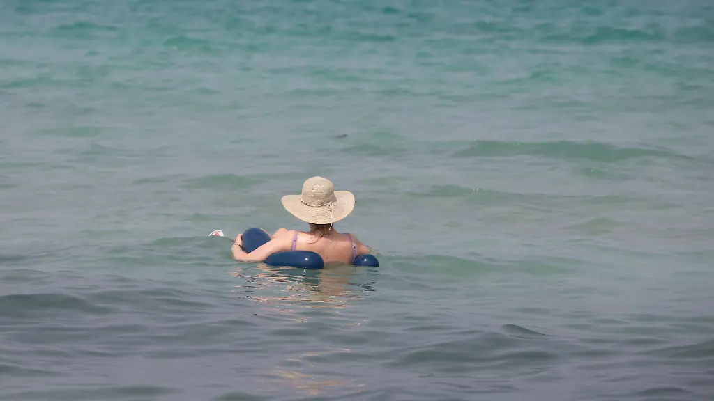 Eine-Person-entspannt-sich-am-Strand-von-Can-Picafort-und-schwimmt-mit-einem-Sonnenhut-auf-dem-Kopf-im-Wasser-an-der-Nordkueste-von-Mallorca
