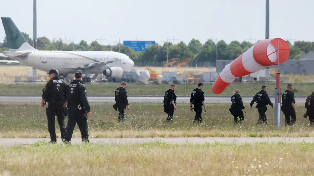Polizisten-gehen-ueber-eine-Wiese-auf-dem-Gelaende-des-Flughafen-Leipzig-Die-Ermittlungen-nach-der-Entdeckung-der-Sprengstoff-Drohne-dauern-an-An-der-noerdlichen-Rollbahn-sind-zahlreiche-Polizistinnen-und-Polizisten-im-Einsatz-und-suchen-das-Gelaende-zu-Fuss-ab