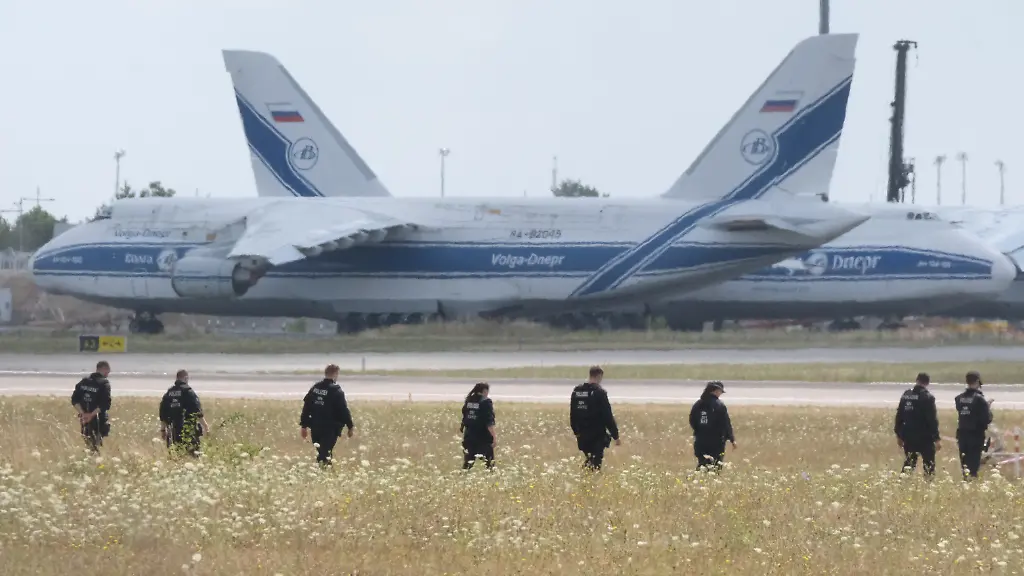 Polizisten-gehen-ueber-eine-Wiese-auf-dem-Gelaende-des-Flughafen-Leipzig-Die-Ermittlungen-nach-der-Entdeckung-der-Sprengstoff-Drohne-dauern-an-An-der-noerdlichen-Rollbahn-sind-zahlreiche-Polizistinnen-und-Polizisten-im-Einsatz-und-suchen-das-Gelaende-zu-Fuss-ab