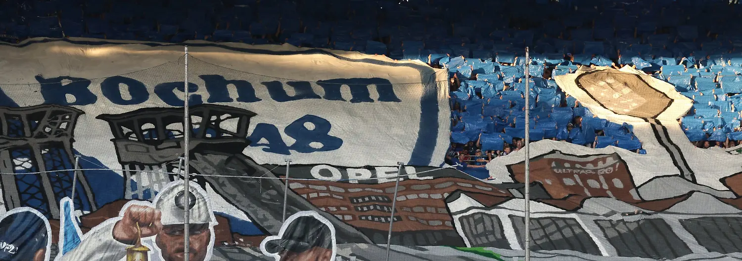 07-08-2026-Nordrhein-Westfalen-Bochum-Fussball-Maenner-2-Bundesliga-VfL-Bochum-Hertha-BSC-1-Spieltag-Vonovia-Ruhrstadion-Das-Team-des-VfL-Bochum-steht-im-Kreis-waehrend-im-Hintergrund-eine-Choreographie-der-Fans-zu-sehen-ist-Foto-David-Ebener-dpa-WICHTIGER-HINWEIS-Gemaess-den-Vorgaben-der-Bundesliga-bzw-des-DFB-Deutscher-Fussball-Bund-ist-es-untersagt-in-dem-Stadion-und-oder-vom-Spiel-angefertigte-Fotoaufnahmen-in-Form-von-Sequenzbildern-und-oder-videoaehnlichen-Fotostrecken-zu-verwerten-bzw-verwerten-zu-lassen
