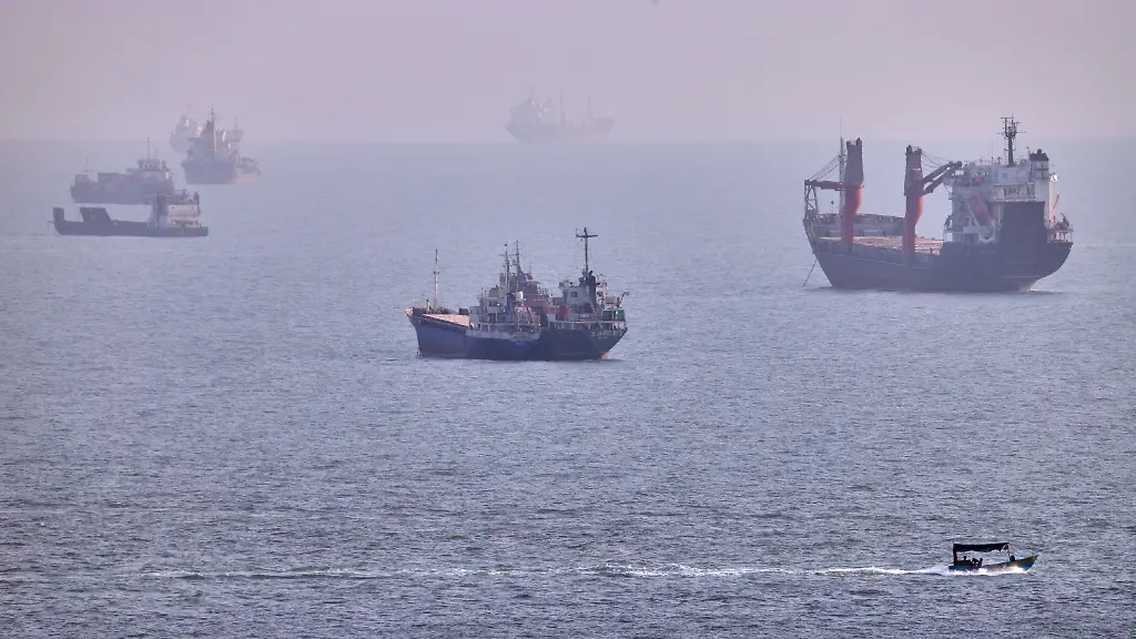 Ein-kleines-Boot-segelt-an-Frachtschiffen-und-anderen-Handelsschiffen-vorbei-die-in-der-Strasse-von-Hormus-vor-Bandar-Abbas-im-Iran-vor-Anker-liegen