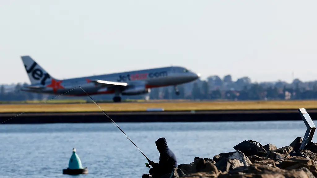 A-person-uses-a-fishing-pole-as-a-Jetstar-plane-takes-off-in-the-background-from-Sydney-International-Airport-in-Sydney-Australia-August-6-2026