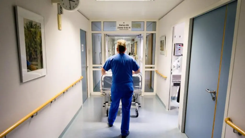 Ein-Krankenpfleger-schiebt-in-einer-Klinik-ein-Krankenbett-durch-den-Flur