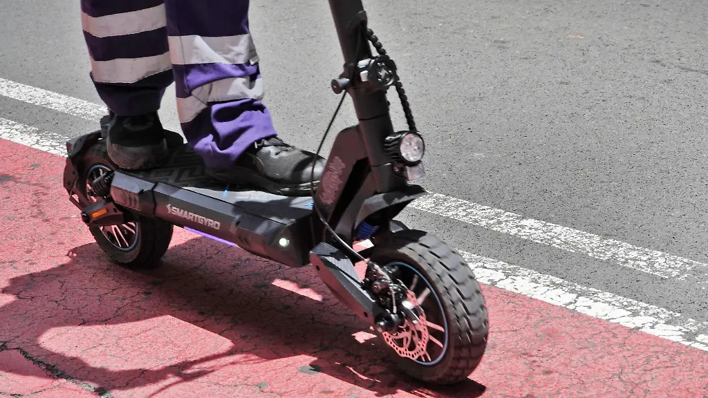 E-Scooter-im-Strassenverkehr-Jugnedlicher-faehrt-mit-einem-Elektroroller-auf-einem-rot-markierten-Radweg-modernes-Fortbewegungsmittel-in-der-Stadt
