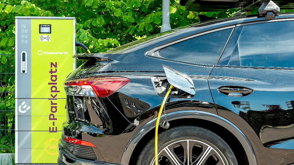 Schleswig-ein-schwarzer-elektrischer-AUDI-auf-einem-E-Parkplatz-in-der-Goethestrasse-beim-Laden-mit-einem-gelben-Ladekabel-an-einer-gruenen-Ladesaeule-der-Stadtwerke-SH-Der-Audi-hat-den-Anschluss-fuer-den-Ladestecker-hinten-auf-der-Beifahrerseite-unter-einer-Verschlussklappe