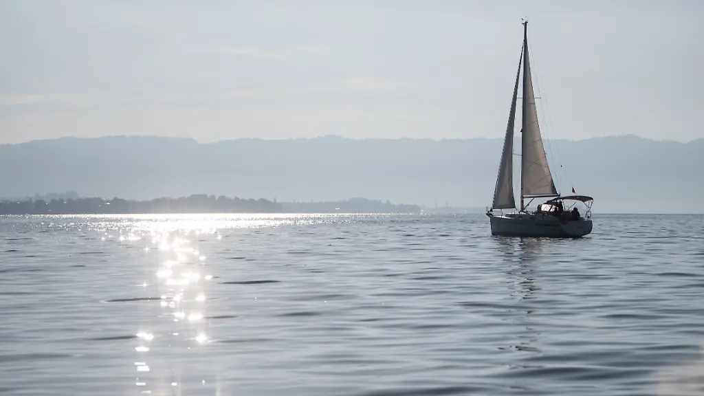 Ein-Segelboot-faehrt-auf-dem-Bodensee-auf-dessen-Wasser-durch-die-Sonne-glitzert-Ein-Prozess-um-ein-toedliches-Schiffsunglueck-auf-dem-Bodensee-bei-dem-eine-57-jaehrige-Deutsche-ums-Leben-kam-soll-neu-aufgerollt-worden