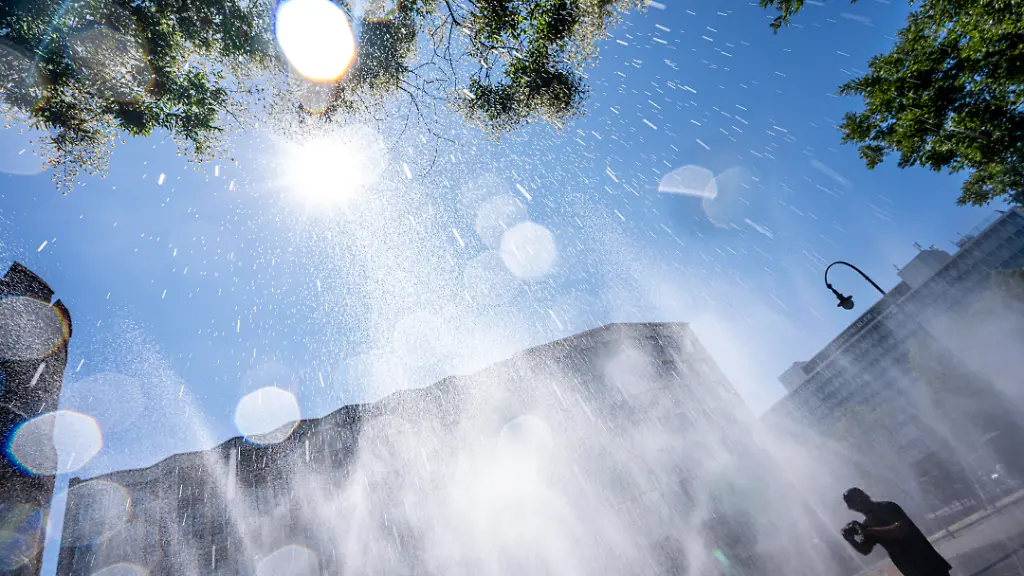 Cooling-Cologne-Aktion-der-Stadt-Koeln-zur-Abkuehlung-von-Hitzebelasteten-Plaetzen-hier-der-Rudolfplatz-in-der-Innenstadt-bei-knapp-37-C-an-dem-Tag-ein-Spruehschlauch-verspritzt-feine-Wassertroepfen-die-die-unmittelbare-Umgebung-einige-Grade-abkuehlt-eine-Aktion-die-bei-extremer-Hitzebelastung-vorgenommen-wird-zur-Anpassung-des-Stadtklimas-an-den-Klimawandel-Passanten-geniessen-den-kuehlenden-Moment-dazu-gibts-Tipps-zum-Umgang-mit-Extremhitze-NRW-Deutschland
