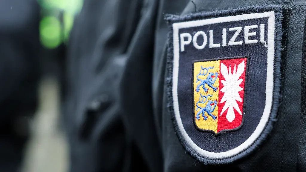 Ein-Logo-der-Polizei-mit-dem-Wappen-von-Schleswig-Holstein-ist-auf-dem-Arm-eines-Beamten-zu-sehen