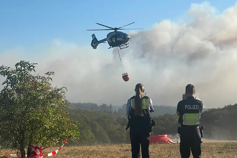 Ein-Polizeihubschrauber-mit-Loeschwasser-Aussenlastbehaelter-startet-zum-Einsatz-bei-den-Loescharbeiten-beim-Waldbrand-im-Huertgenwald-Mehrere-Hundert-Hektar-Waldflaeche-stehen-in-Flammen