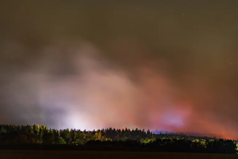 Naechtliche-Loescharbeiten-am-Waldbrand-im-Huertgenwald-bei-Kleinhau-Nachtaufnahme-aus-Kleinhau-Gemeinde-Huertgenwald-Kreis-Dueren-Die-Loescharbeiten-am-Grossbrand-im-Huertgenwald-laufen-auch-in-der-Nacht-auf-Hochtouren-rund-500-Einsatzkraefte-loesen-sich-im-12-Stunden-Rhythmus-ab-Eine-Mischung-aus-Flammenschein-Scheinwerferlicht-und-Blaulicht-taucht-den-aufsteigenden-Brandrauch-in-ein-dramatisches-Licht