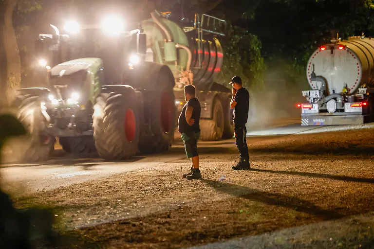 Fahrer-von-Traktoren-stehen-am-Strassenrand-und-schauen-Traktoren-mit-Wasser-befuellten-Anhaengern-zu-die-die-Feuerwehr-beim-Loeschen-des-Waldbrands-unterstuetzen-Hunderte-Feuerwehrkraefte-kaempfen-auch-in-der-Nacht-weiter-gegen-den-grossen-Waldbrand-im-Huertgenwald-in-der-Eifel