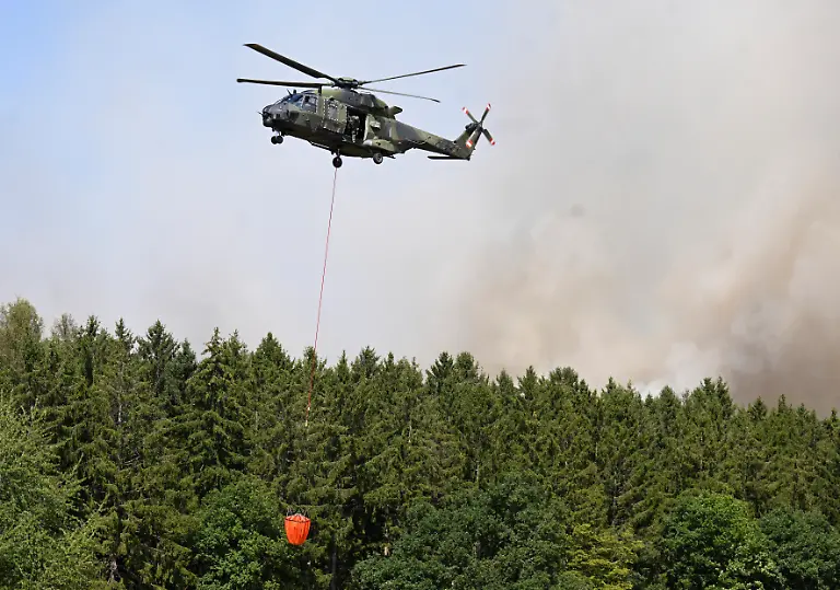 A-German-armed-helicopter-loads-water-to-fight-a-forest-fire-in-Huertgenwald-western-Germany-Friday-August-14-2026-Around-1-800-people-had-to-leave-their-homes-in-western-Germany-overnight-as-a-wildfire-spread-nearby-officials-said-with-helicopters-and-army-equipment-deployed-to-help-battle-the-flames-A-district-of-the-town-of-Huertgenwald-near-the-Belgian-and-Dutch-borders-was-evacuated-after-the-fire-expanded-from-25-hectares-around-60-acres-to-300-hectares-by-Friday-morning