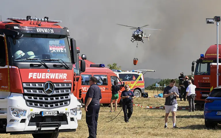 A-police-helicopter-loads-water-to-fight-a-forest-fire-as-firefighters-work-in-Huertgenwald-western-Germany-on-August-14-2026-where-around-1-800-people-had-to-leave-their-homes-overnight-as-a-wildfire-spread-nearby-A-district-of-the-town-of-Huertgenwald-near-the-Belgian-and-Dutch-borders-was-evacuated-after-the-fire-expanded-from-25-hectares-around-60-acres-to-300-hectares-by-Friday-morning-Residents-were-urged-to-take-only-the-most-important-personal-items-with-them-as-the-fire-draws-nearer-a-spokeswoman-for-the-local-district-told-AFP